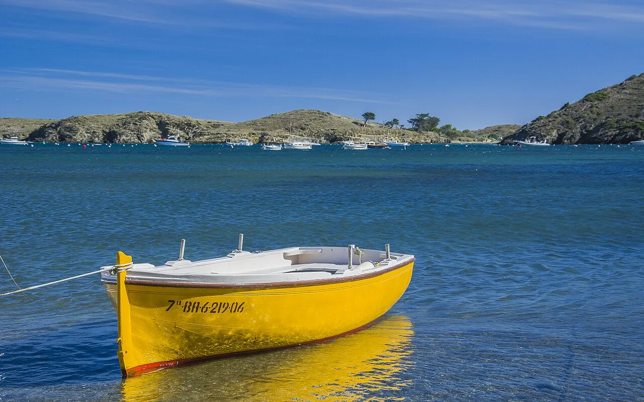 Ein gelbes hölzernes Fischerboot, vertäut im klaren Wasser der Bucht von Portlligat